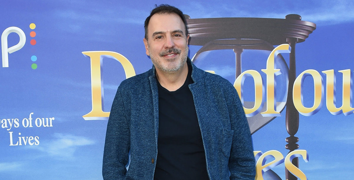 days of our lives head writer ron carlivati in black t-shirt blue jacket against days backdrop