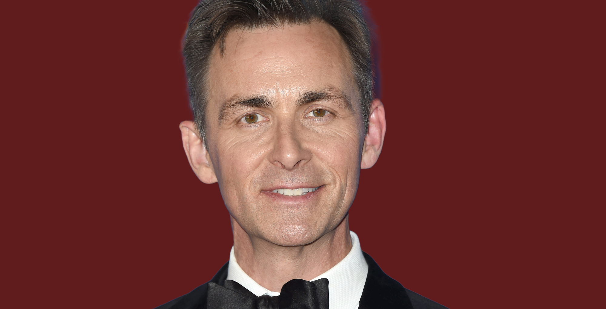 james patrick stuart of general hospital in a tux against a red background.