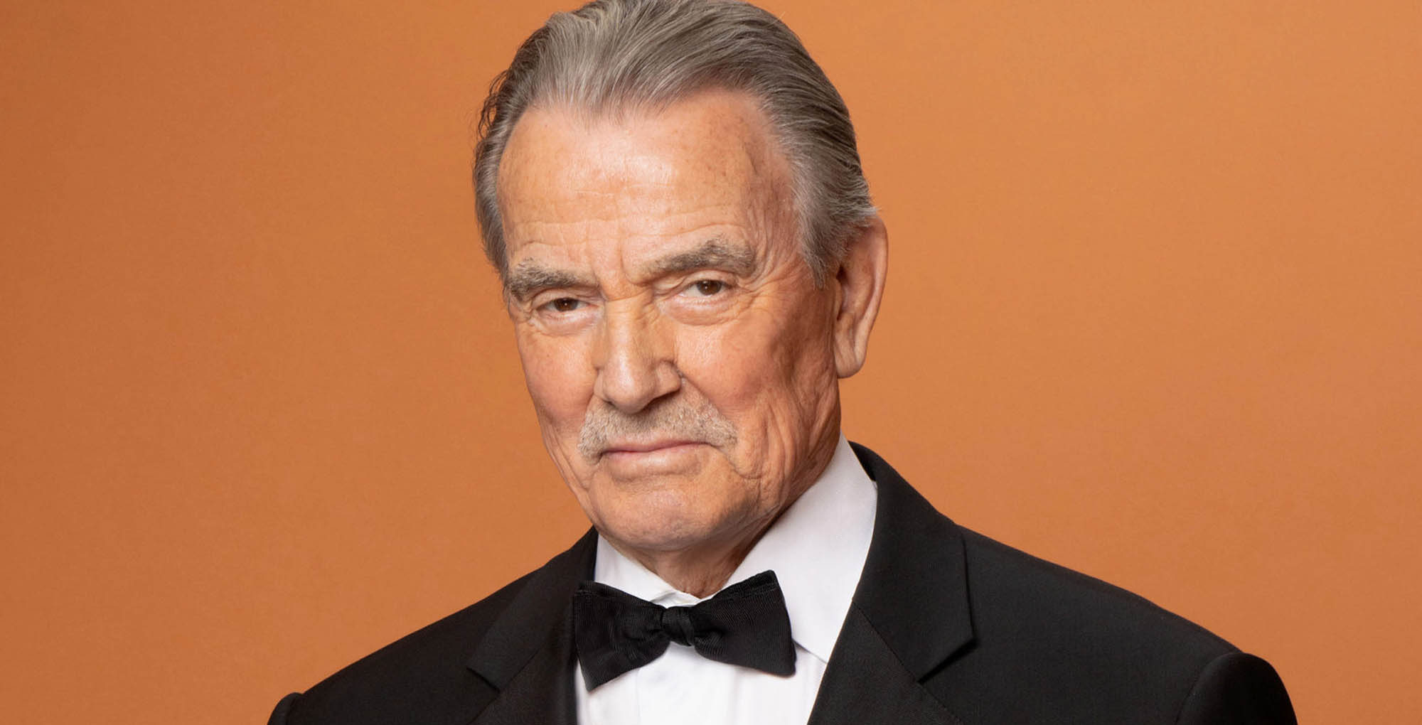 young and the restless star eric braden wearing a tux against an orange background.